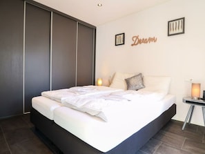 Ein modernes Schlafzimmer mit einem großen Bett, dunklen Schiebetüren und einer Wandlampe.