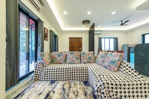 A modern living room with a sofa set, large windows, and a ceiling fan. - Ansh Villa Luxury 4-BHK Pet-friendly (Jambrung)