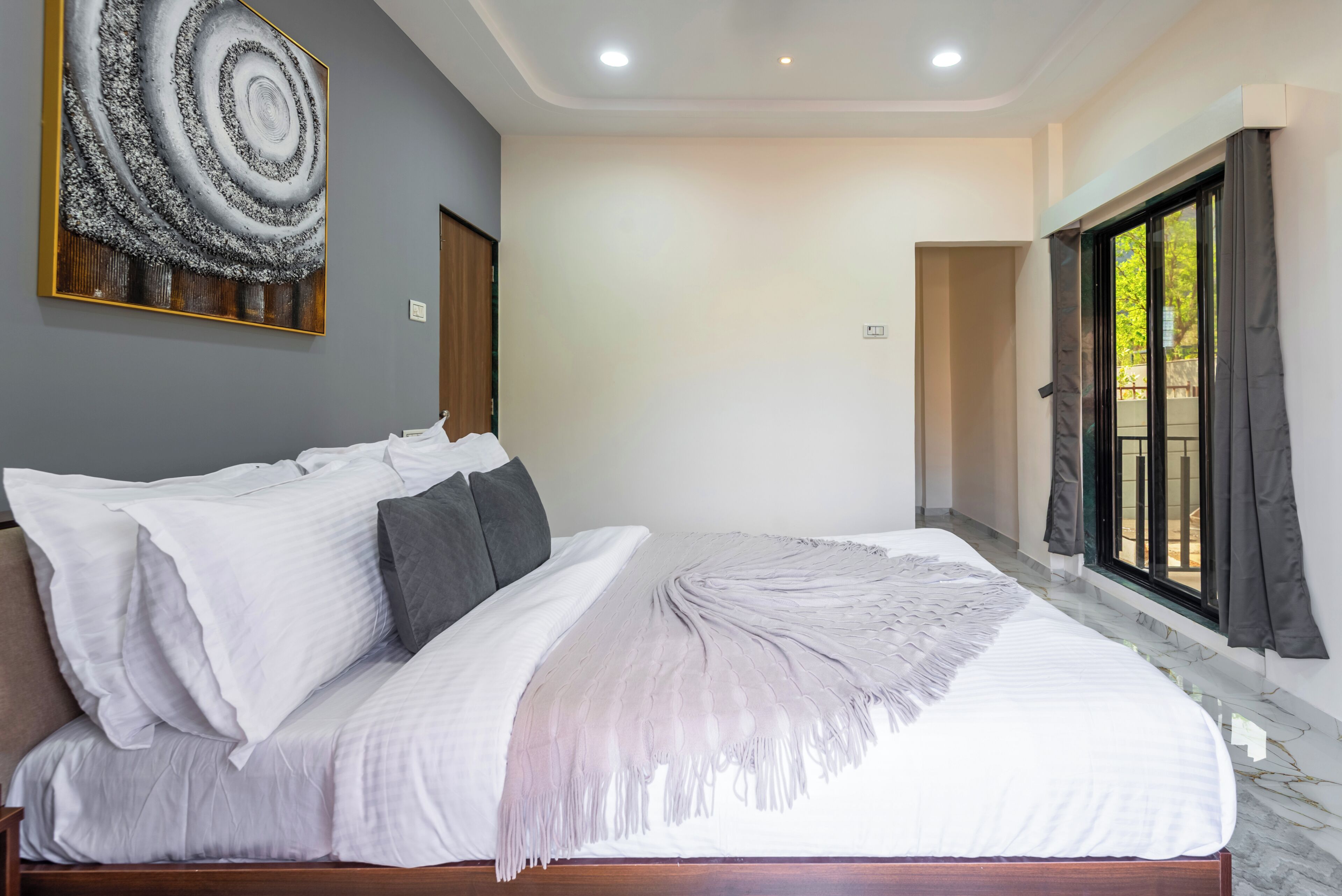 A modern bedroom with a large bed, a wall art piece, and a view through a window.