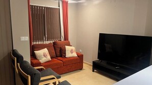 Una sala de estar con sofá, dos sillones, televisor y una ventana con cortinas.