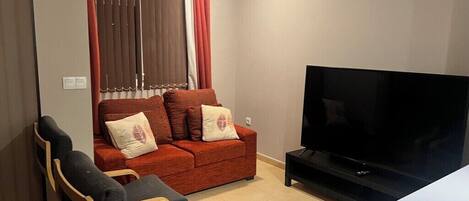 A living room with a sofa, two armchairs, a TV, and a window with curtains.