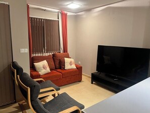 A living room with a sofa, two armchairs, a TV, and a window with curtains.