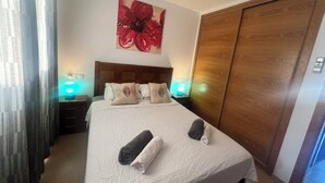 Habitación de hotel con una cama, dos lámparas de noche, un armario de madera y un cuadro grande con motivos florales en la pared.