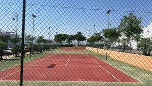 Una cancha de tenis rodeada por una cerca de malla metálica, con un cielo despejado.