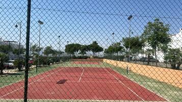 Un terrain de tennis entouré d’une clôture en treillis métallique, avec un ciel dégagé au-dessus.