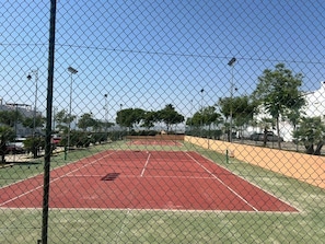 A tennis court enclosed by a chain-link fence with a clear sky above.