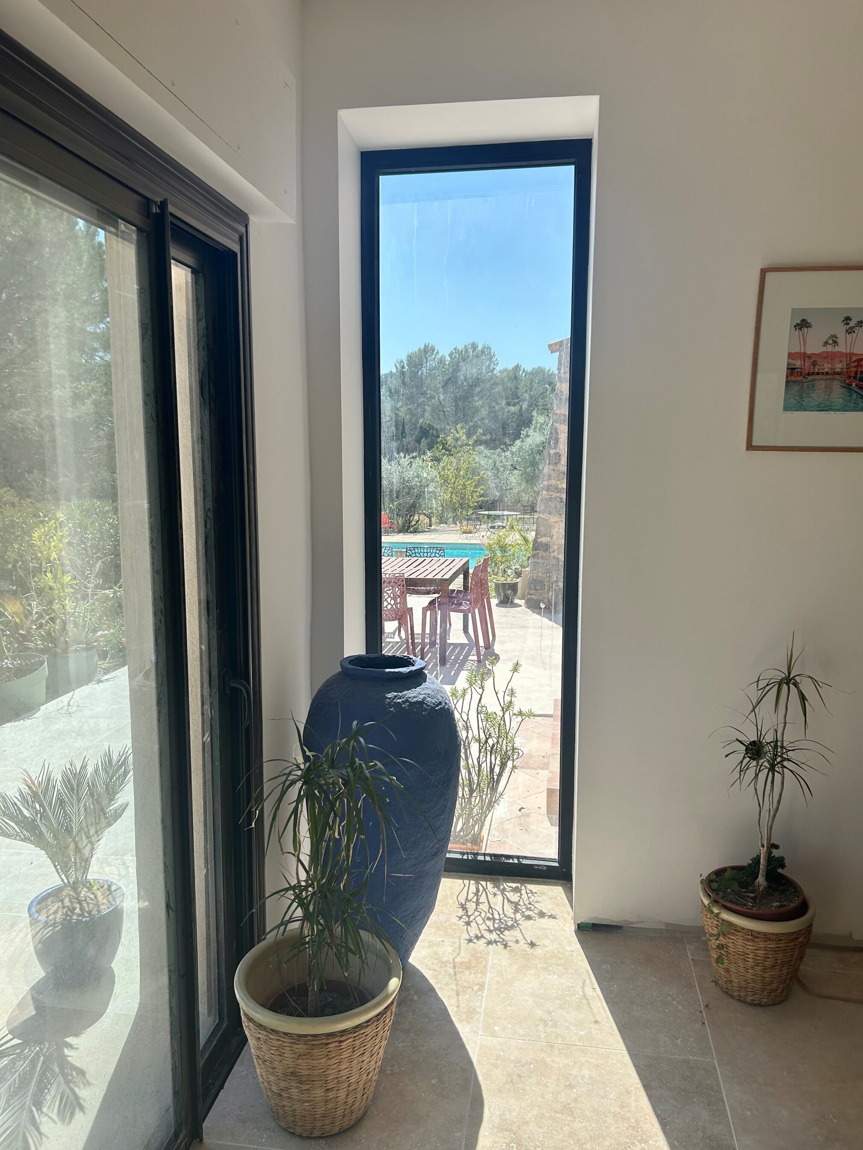 Una habitación con un ventanal amplio, una puerta que da al exterior y plantas en macetas.
