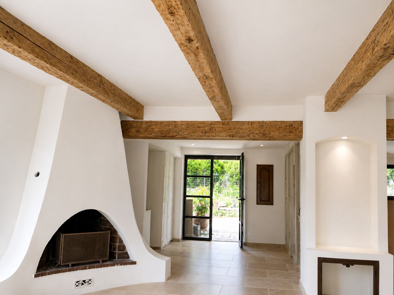 Un interno spazioso con travi a vista in legno, un camino e vista su una zona esterna attraverso una porta in vetro.