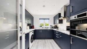 Een moderne keuken met donkere kastjes, een ingebouwde wasmachine en een groot raam met uitzicht op de omgeving.