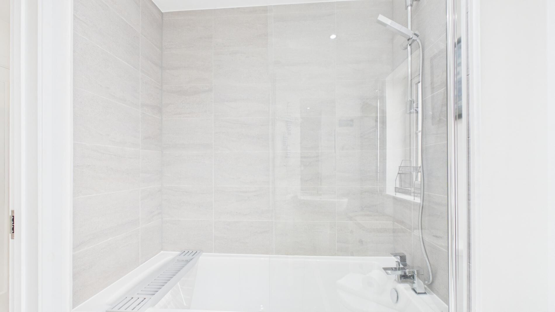 A modern bathroom with a bathtub, shower, and tiled walls.
