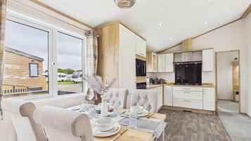 Una cocina moderna con armarios blancos, una zona de comedor con una mesa dispuesta para cuatro personas y vistas a un edificio de madera.