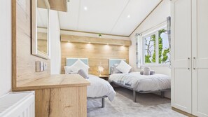 Een slaapkamer met twee bedden, een houten hoofdbord, een nachtkastje, een radiator en een raam met uitzicht op bomen.