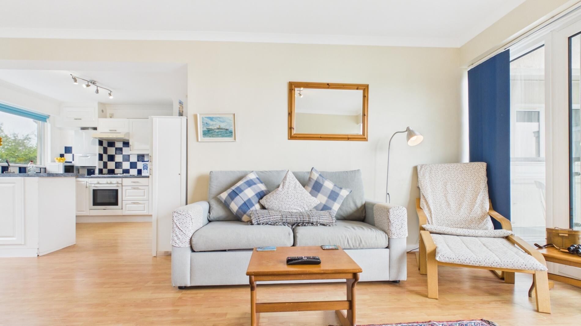 A modern living room with a sofa, a coffee table, a chair, a mirror, and a kitchen in the background.