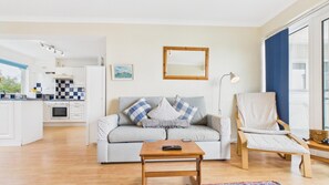 Ein modernes Wohnzimmer mit Sofa, Couchtisch, Sessel, Spiegel und einer Küche im Hintergrund.