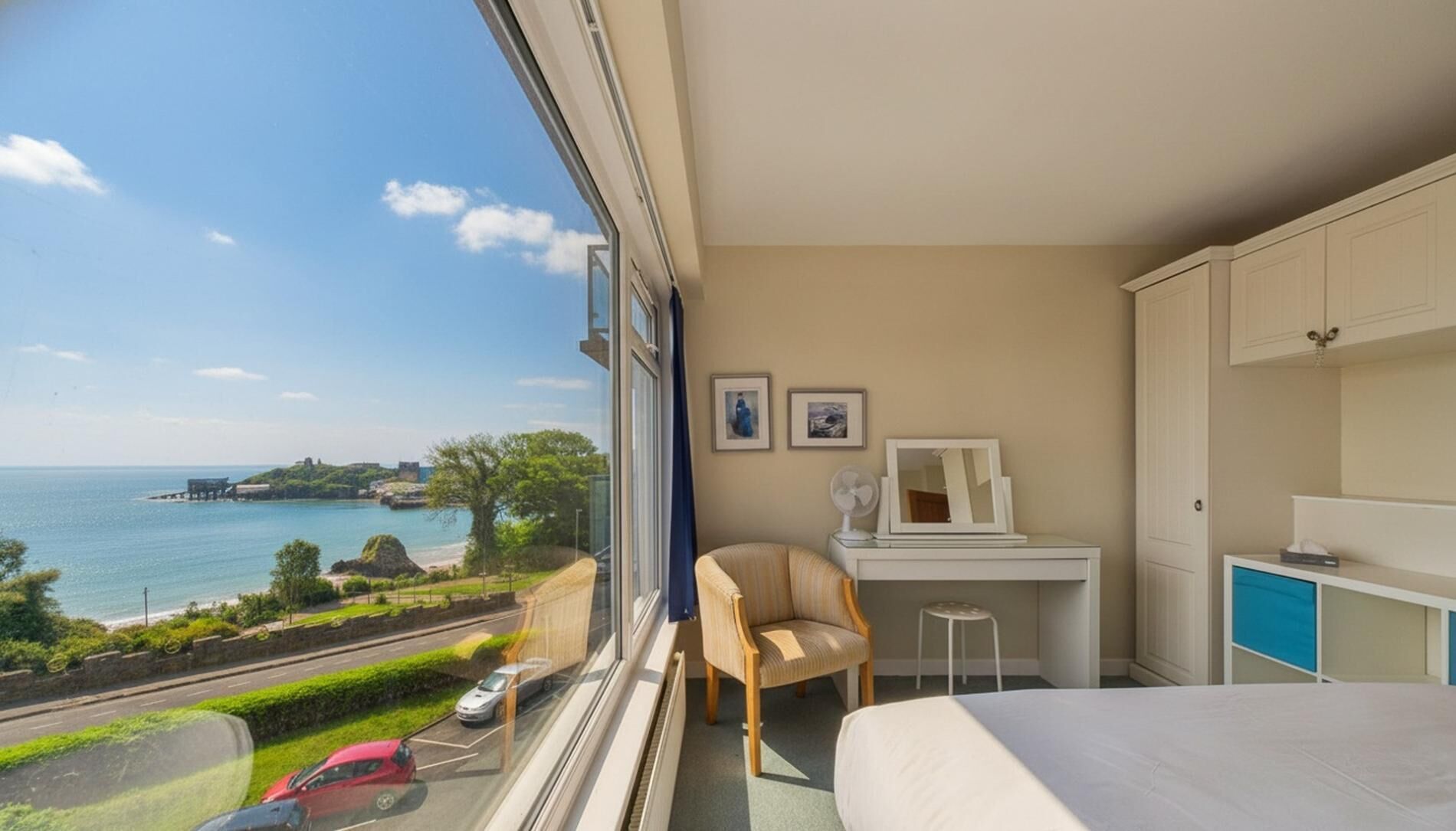 A hotel room with a large window, a bed, a desk, a chair, and a dresser.