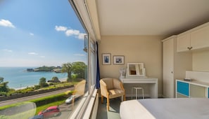 Ein Hotelzimmer mit großem Fenster, einem Bett, einem Schreibtisch, einem Stuhl und einer Kommode.
