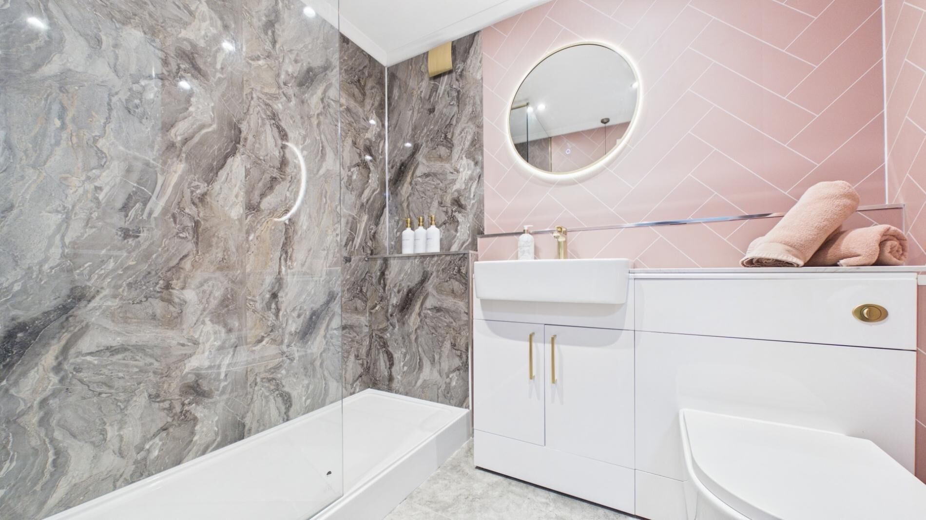 A bathroom with a marble wall, a white sink, a toilet, and a bathtub.