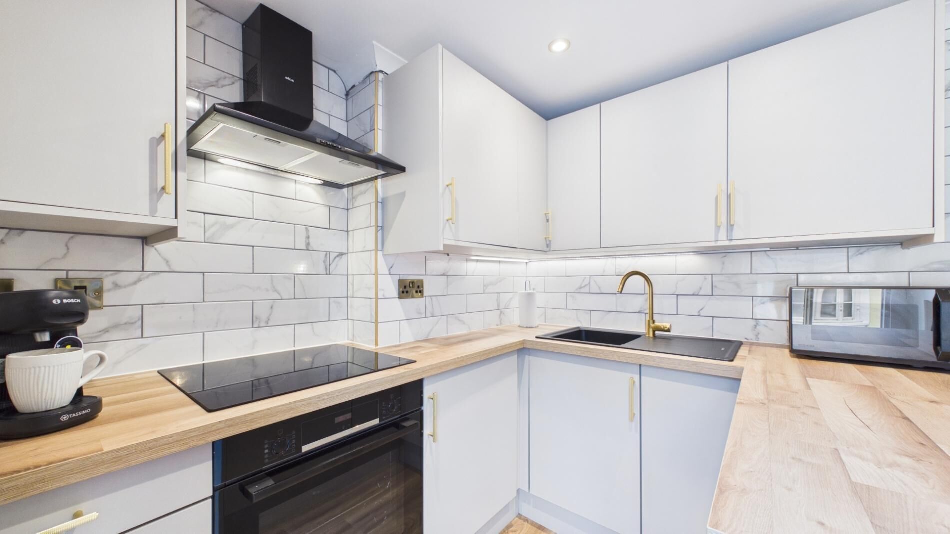 A modern kitchen with white cabinets, a black stove, and a wooden countertop.