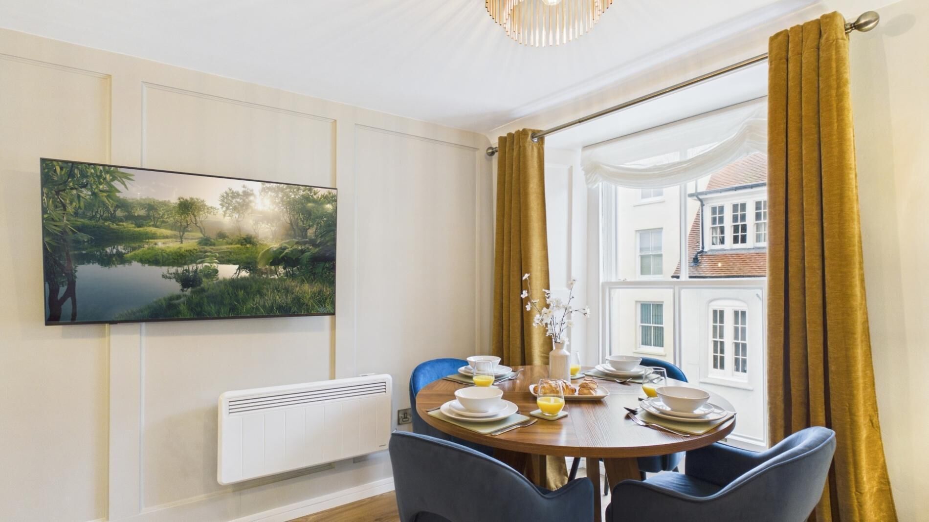 A dining room with a table set for breakfast, a painting on the wall, and a window with curtains.