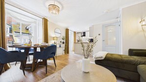 A modern living room with a dining area, a sofa, a coffee table, and a kitchen in the background. - Harbour Rose - 1 Bedroom Apartment - Tenby (Tenby)