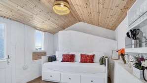 Ein Schlafzimmer im Loft-Stil mit weißen Wänden, Holzbalkendecke, einem Bett mit Stauraum und einem Regal mit Küchenutensilien.