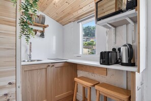 Eine kleine Küche mit Holzschränken, einem Fenster und einer Arbeitsplatte mit Wasserkocher und Toaster.