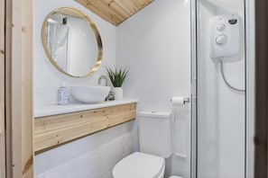 Ein Badezimmer mit weißem Waschbecken, einem Spiegel mit goldener Rahmung, einer Toilette und einer Duschkabine.