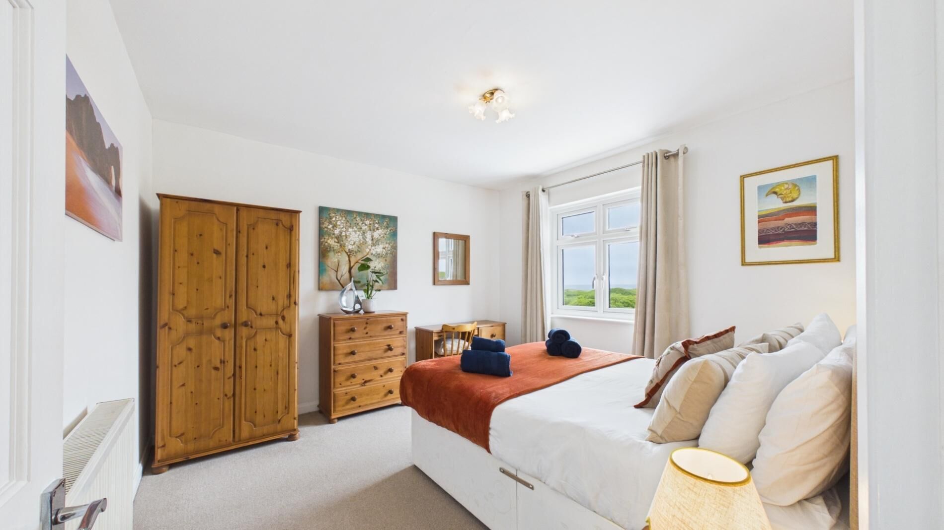 Ein Schlafzimmer mit Bett, Kommode, Schreibtisch, Fenster mit Blick und Kleiderschrank.