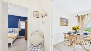 A room with a bed, a dining table with chairs, a view of the outdoors, and a painting on the wall. - St Catherines Apartment - 2 Bedroom - Penally (Tenby)