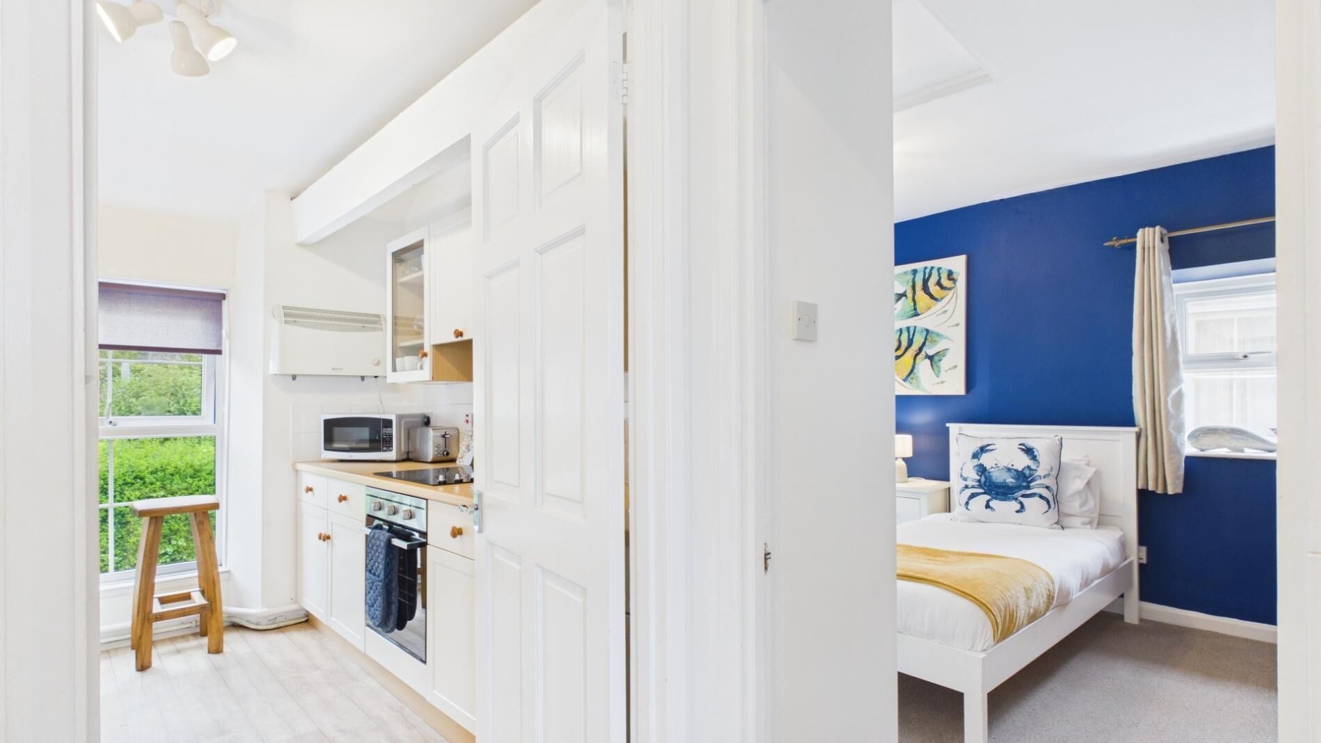 Una habitación con cama, ventana con cortinas, un cuadro y una kitchenette con microondas y tostadora.