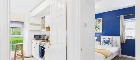 Una habitación con cama, ventana con cortinas, un cuadro y una kitchenette con microondas y tostadora.