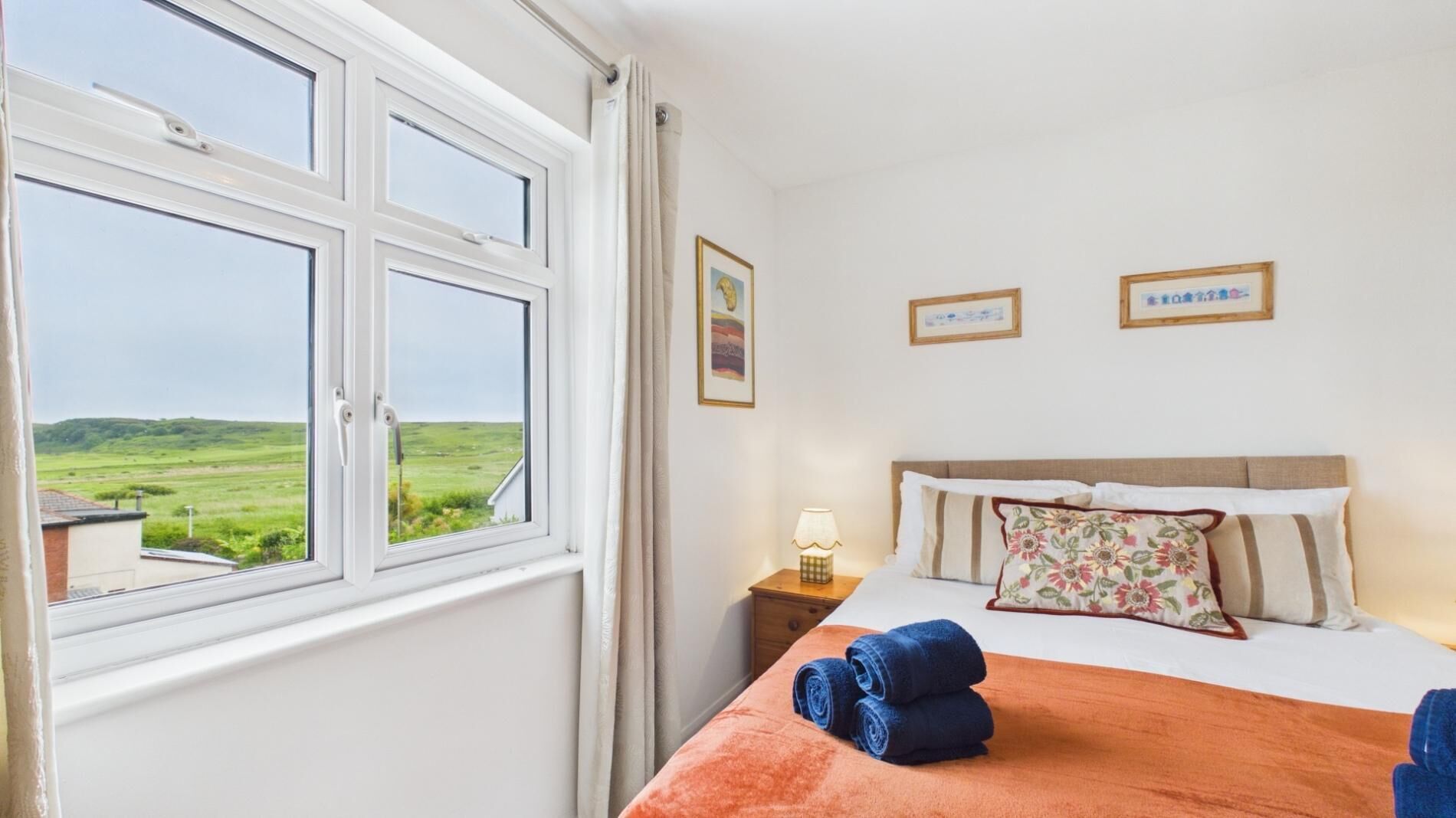 A bedroom with a bed, a nightstand, a lamp, and a window with a view of a green landscape.