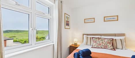 A bedroom with a bed, a nightstand, a lamp, and a window with a view of a green landscape.