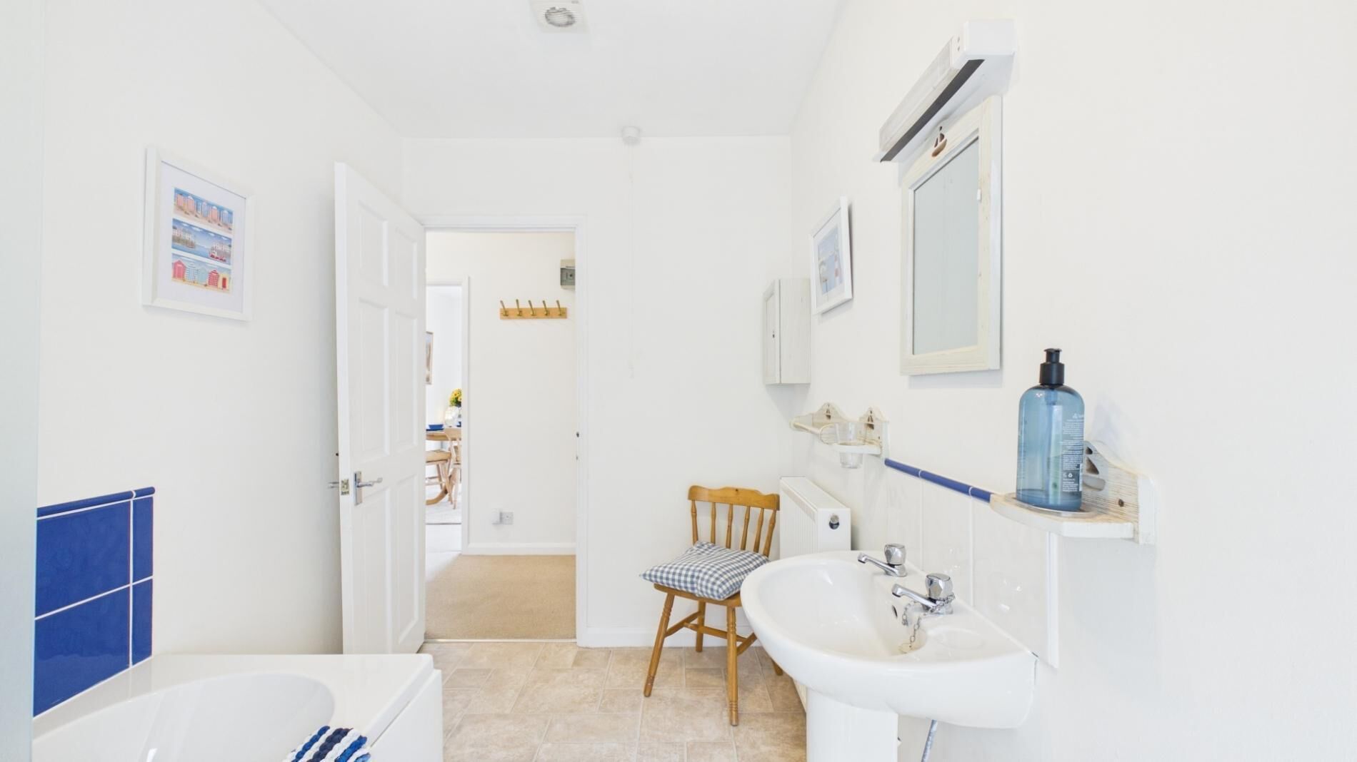 Een badkamer met een bad, wastafel en stoel. Er is een deur naar een andere kamer.