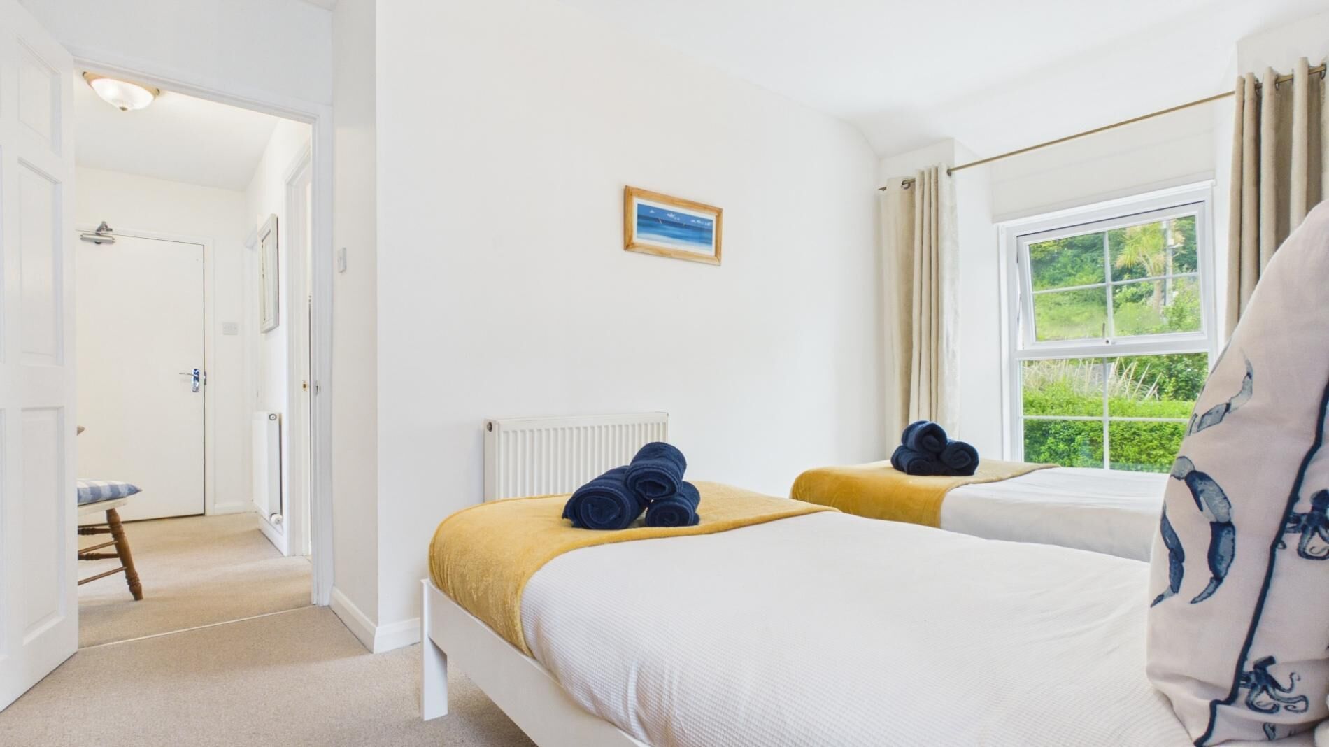 Een slaapkamer met twee bedden, een radiator, een raam met gordijnen en een deur naar een badkamer.