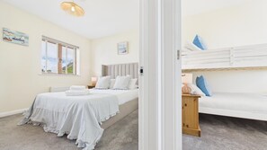 A bedroom with a bed, a bedside table, a lamp, and a window with blinds. - Anchors Aweigh - 2 Bedroom - New Hedges (Saundersfoot)