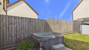 Ein Garten mit Holzzaun, Whirlpool und einem kleinen Tisch mit Flasche und Gläsern.