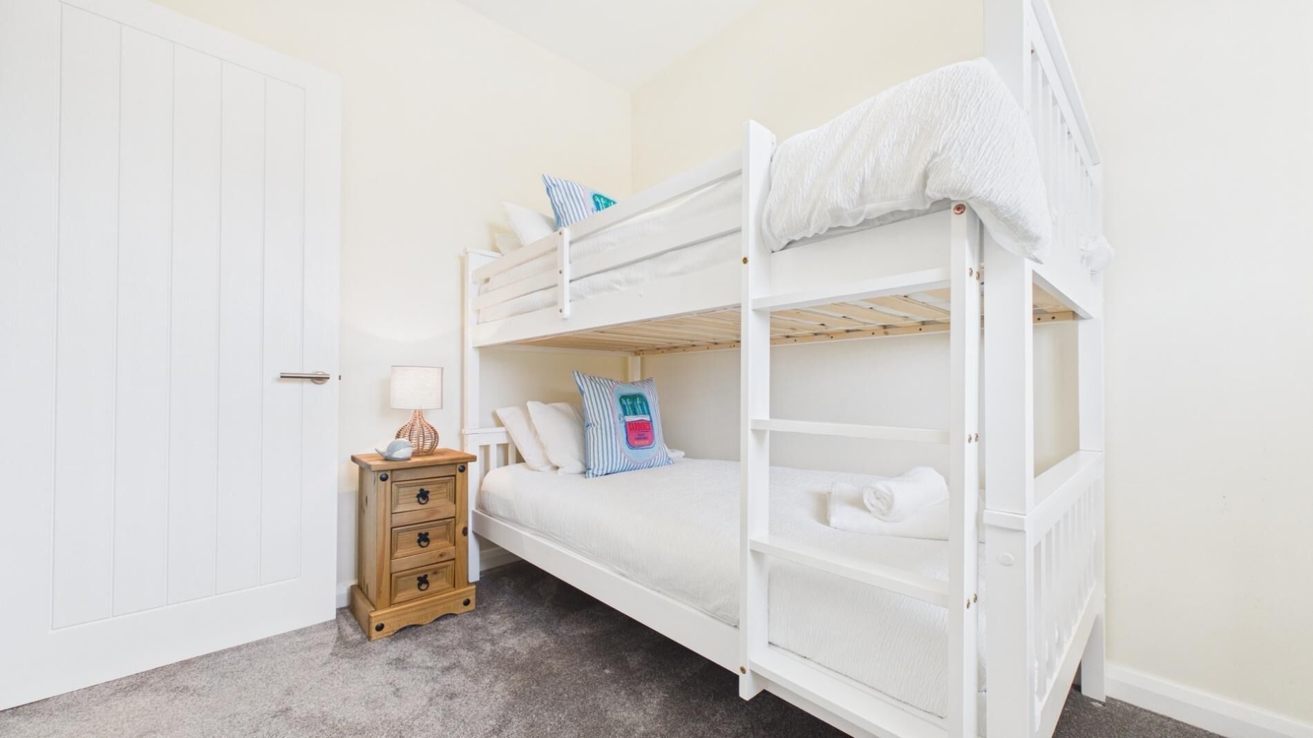 A bunk bed room with a wooden nightstand, a lamp, and a door.