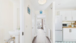 A narrow hallway leading to a kitchen with white cabinets, a microwave, and a sink. - Anchors Aweigh - 2 Bedroom - New Hedges (Saundersfoot)