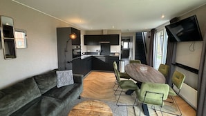 Una sala de estar moderna con un sofá, una mesa de comedor con sillas, una zona de cocina y un televisor montado en la pared.