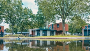 Un edificio moderno reflejado en un cuerpo de agua tranquilo, rodeado de árboles.