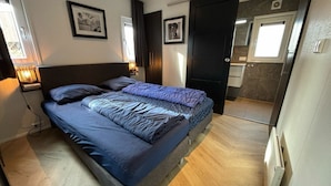 Un dormitorio con cama, mesitas de noche, armario y baño visible a través de una puerta abierta.
