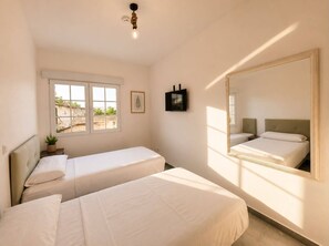 Un dormitorio con dos camas, una ventana, un televisor de pared y un foco en el techo.
