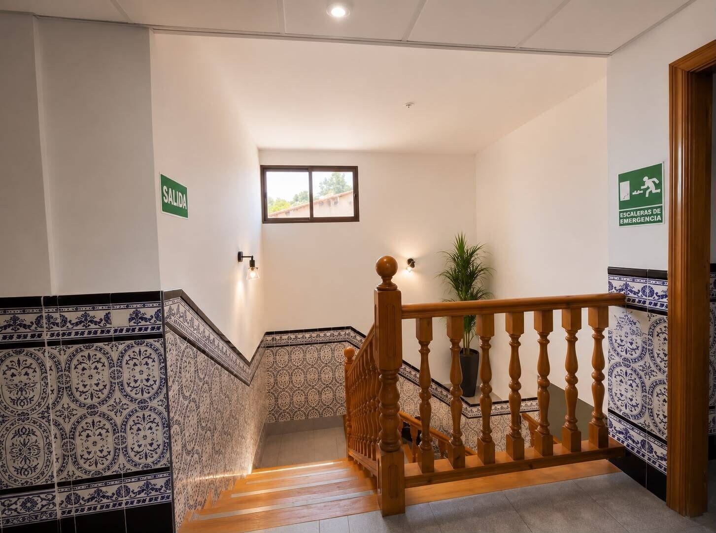 A staircase with patterned tiles, a wooden handrail, and emergency exit signs.