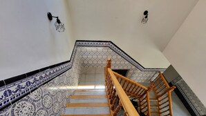 A staircase with patterned tiles, wooden handrails, and wall-mounted light fixtures.