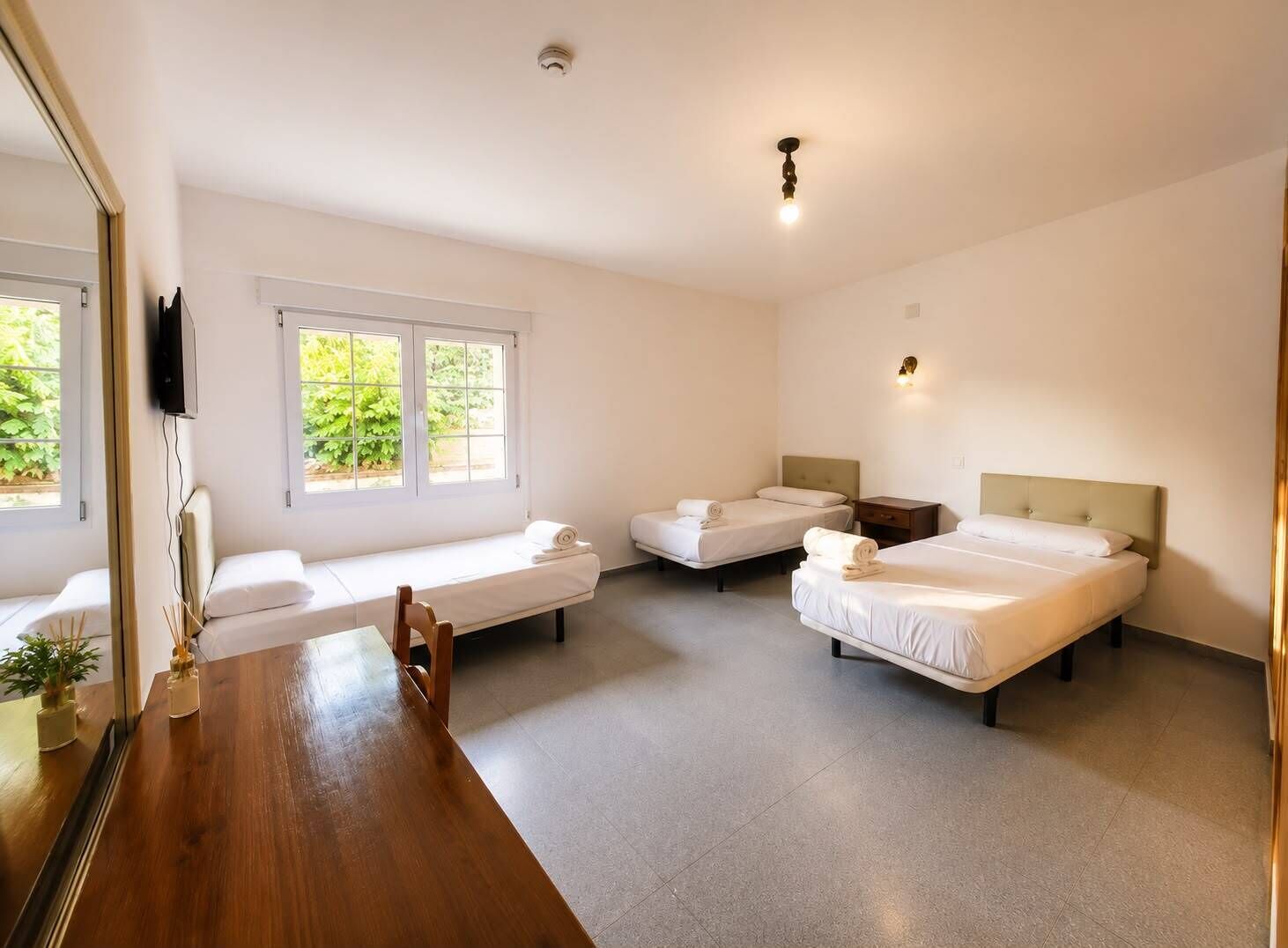Een hotelkamer met twee bedden, een houten tafel en een aan de muur bevestigde televisie.