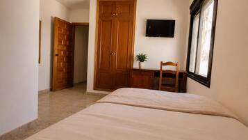 Een slaapkamer met een bed, een houten garderobe, een bureau met stoel, een televisie en een raam.