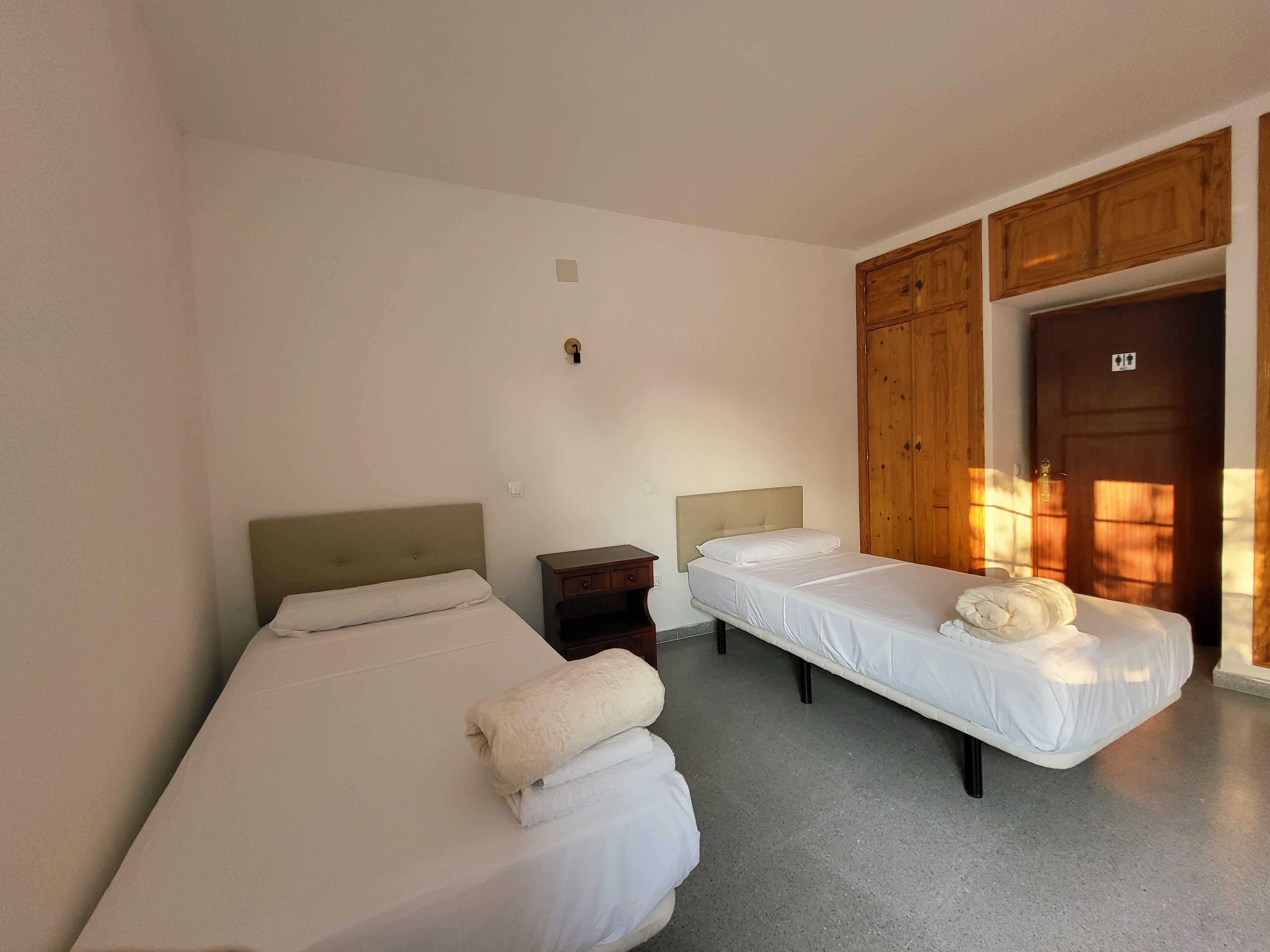 A room with two beds, a wooden wardrobe, and a door.