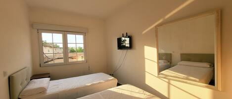 A room with two beds, a large mirror, a television, and a window.