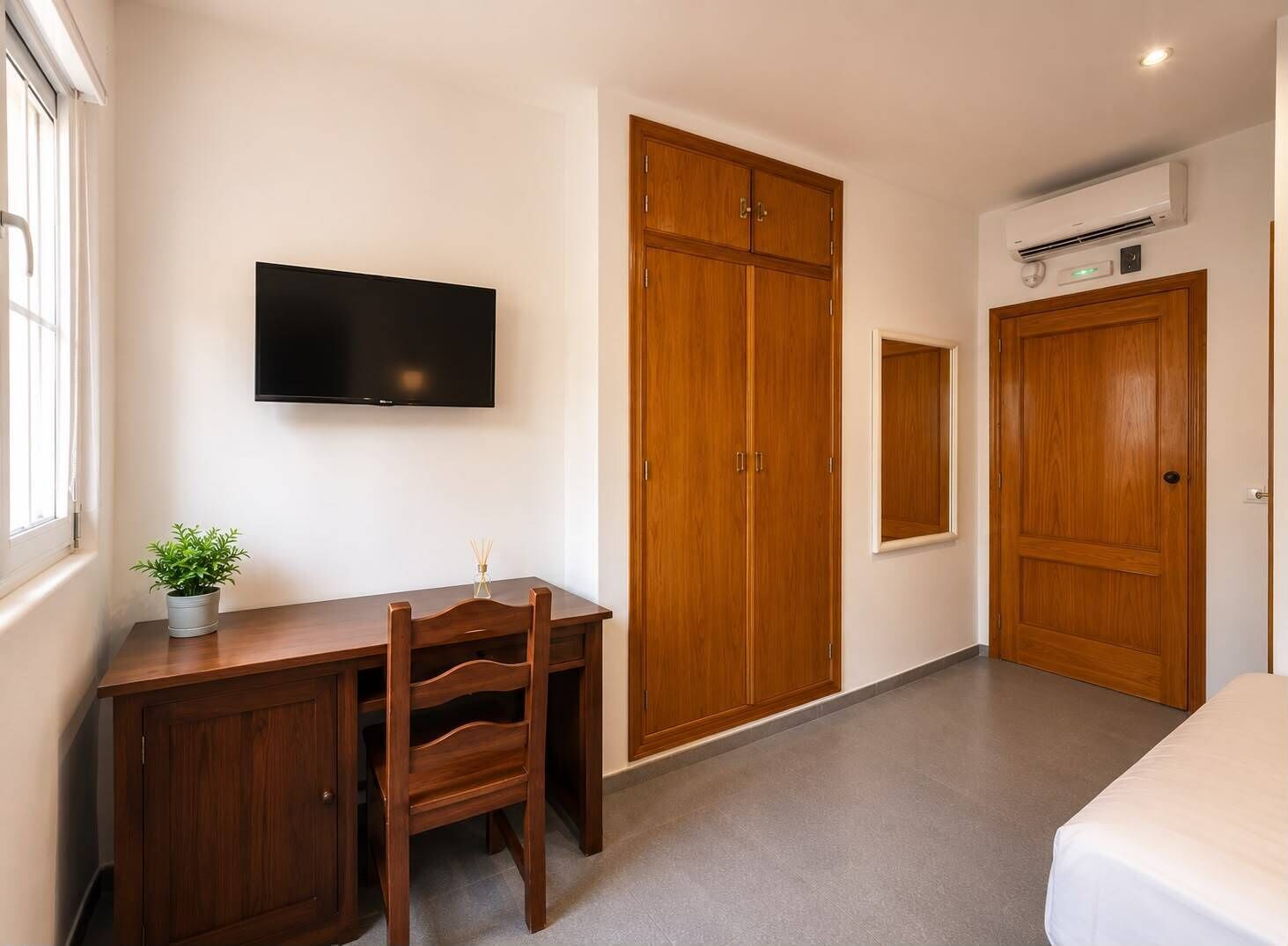 A bedroom with a bed, a desk with a chair, a television, and wooden wardrobes.